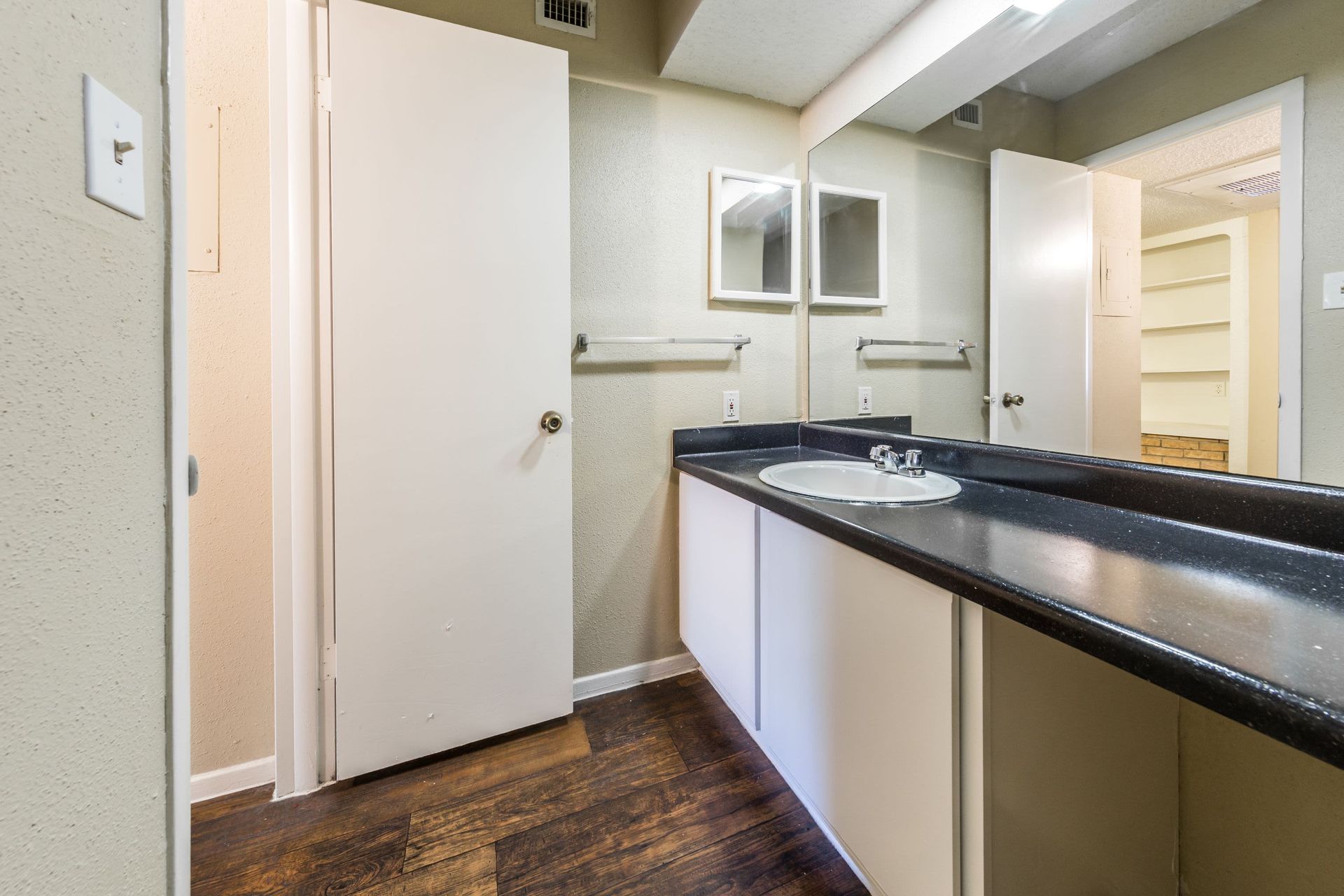Apartment bathroom with a sink, mirror, and wooden floor at SoCo on the Lake in Austin, TX.