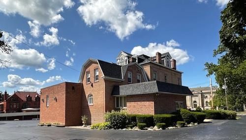 Brick building with mansard roof and chimney beside a parking lot under a blue sky