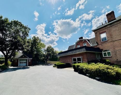 Sunny courtyard with brick buildings, trimmed hedges, and a wide paved driveway under a blue sky