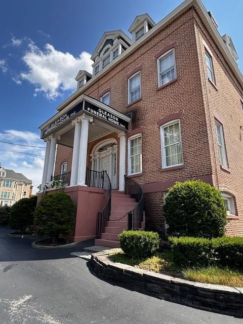 Brick building with white columns and steps, viewed from below on a sunny day.