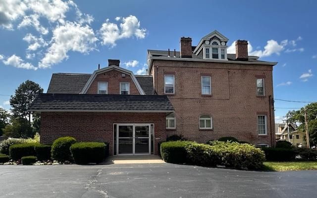 Brick building with a covered entrance, hedges, and a small tower under a blue sky