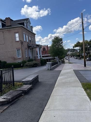 Sidewalk beside brick row houses and a low stone wall under a blue sky with clouds
