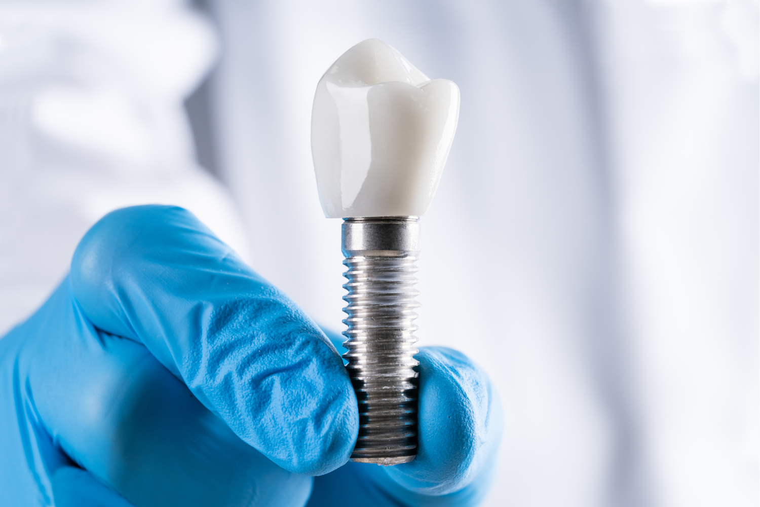 Dentist holding a dental implant; shows a metal screw and a white tooth crown.