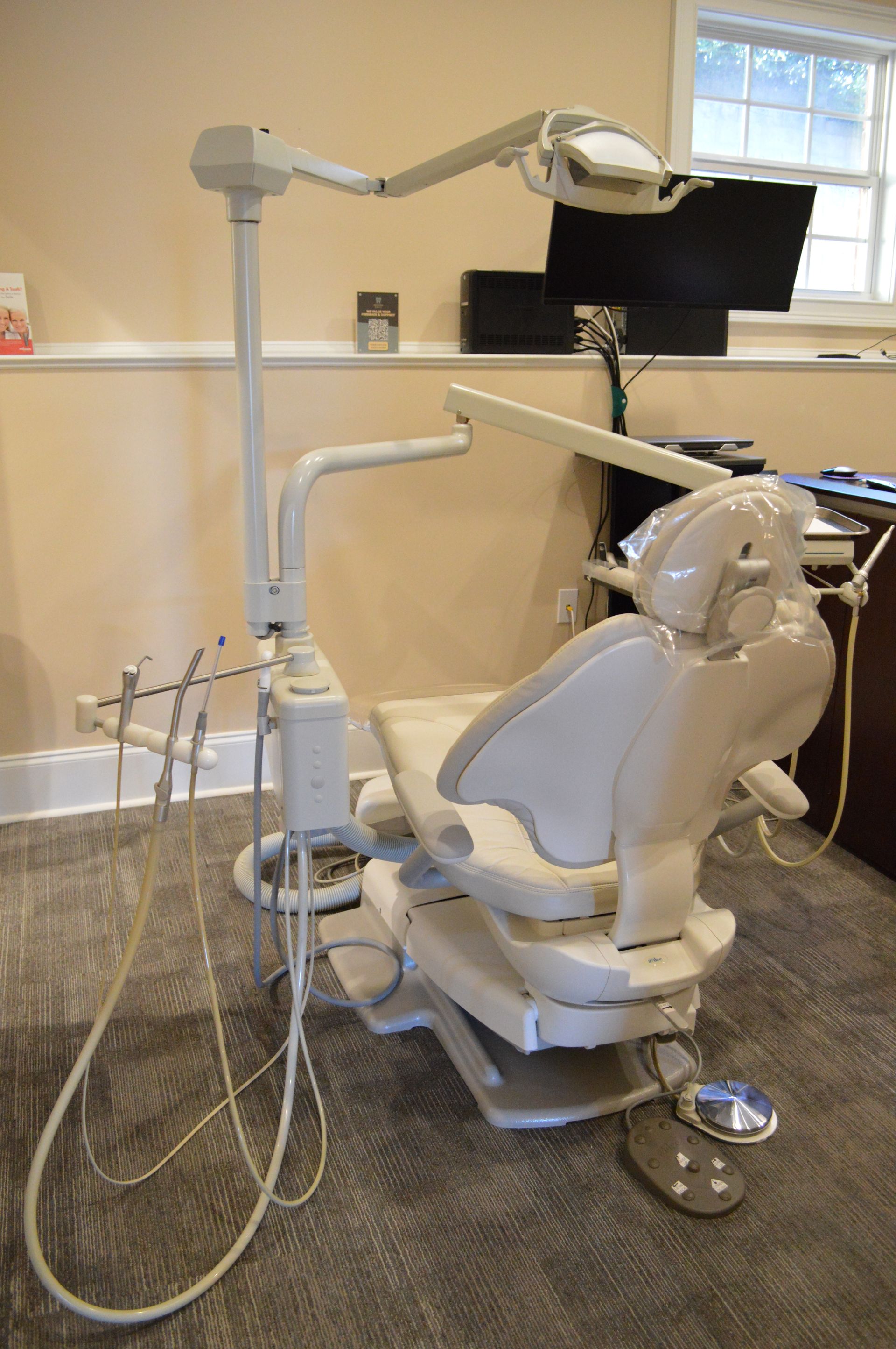 Dental chair with attached light and instruments, in a dentist's office.