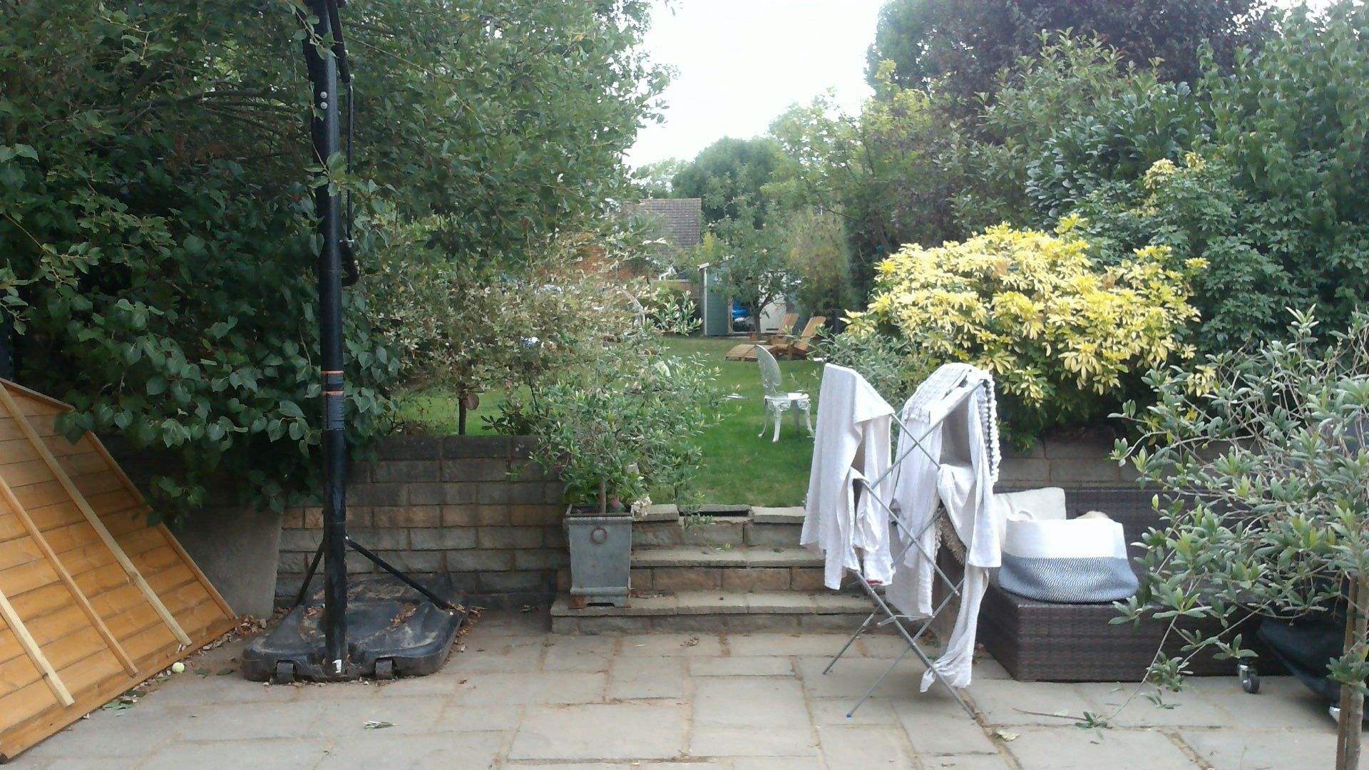 Backyard with clothes drying on a rack, stone patio, steps, green grass, trees, and a house in the background.