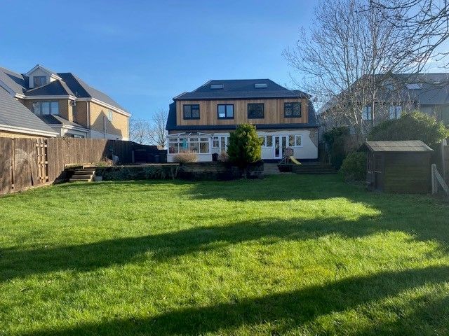 Backyard view of a two-story house with a wooden facade, green lawn, and sunny sky.