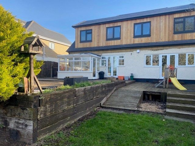 Backyard with wooden retaining wall, lawn, patio, and house with wood siding.