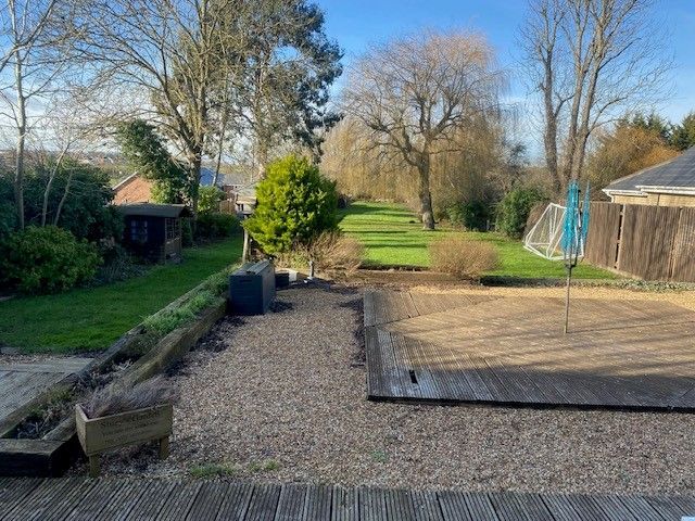Backyard with gravel path, deck, lawn, and trees under a sunny sky.