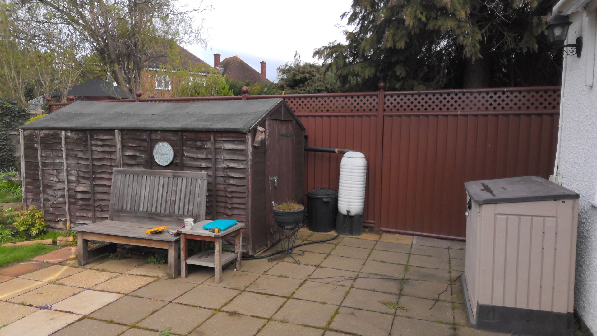 Backyard with a wooden shed, bench, brown fence, and a water butt.