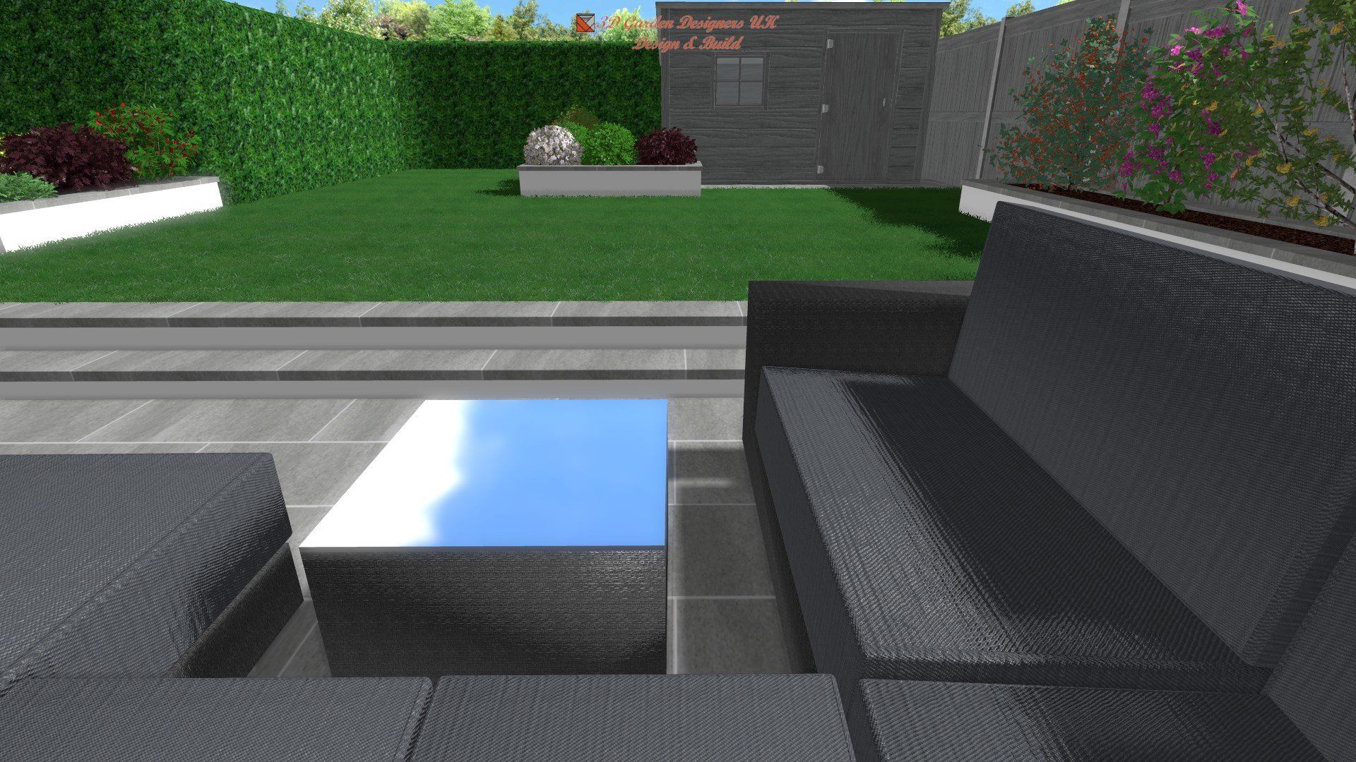 Outdoor patio with dark gray sectional sofa and reflective square coffee table. Green lawn and hedge in background.