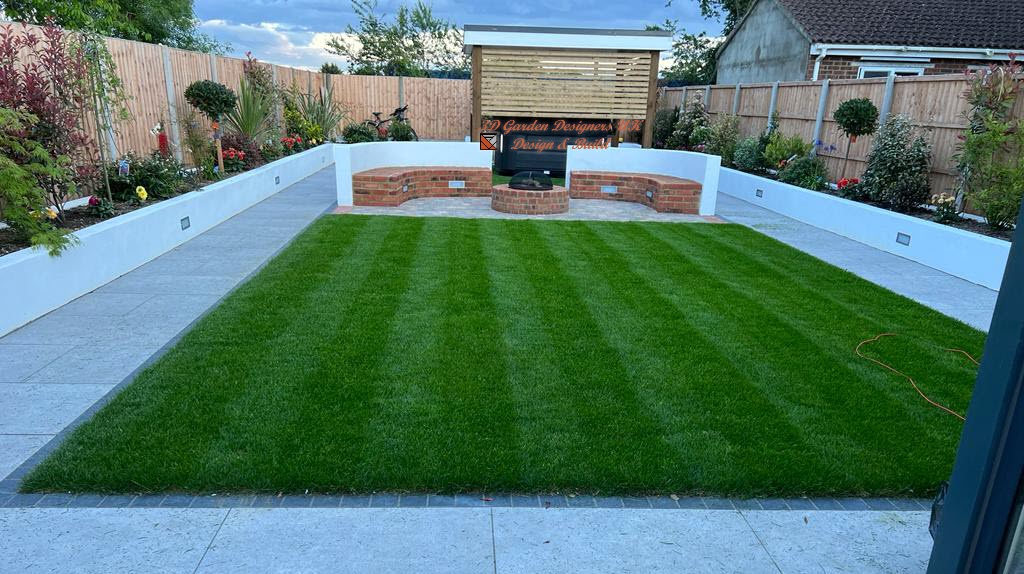 Neat, green lawn in a rectangular garden with brick and white walls, bench, and wooden structure.