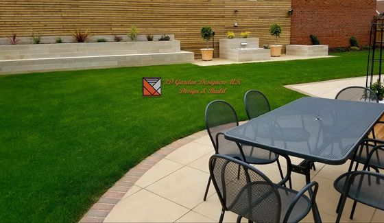Green lawn, patio with table and chairs, planters, and a wooden fence.