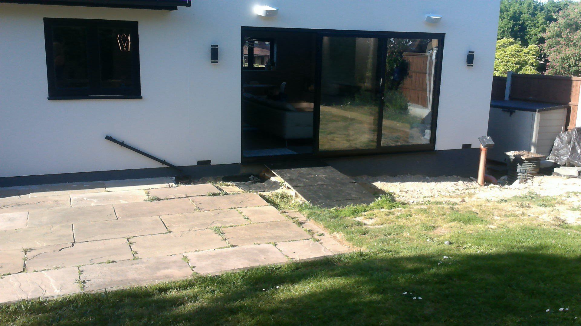 White building with a sliding glass door and a paved patio leading to a grassy yard.