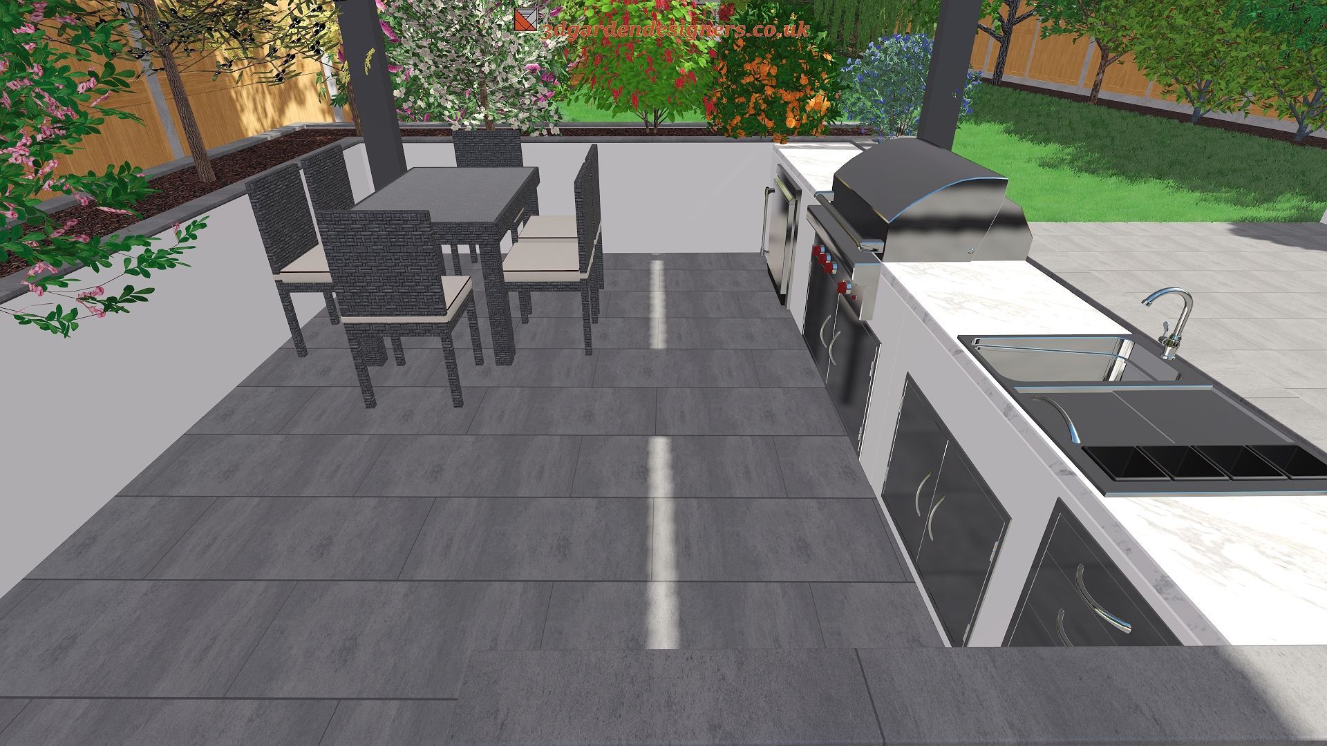 Outdoor kitchen with gray stone patio, table, chairs, grill, and sink against a garden backdrop.