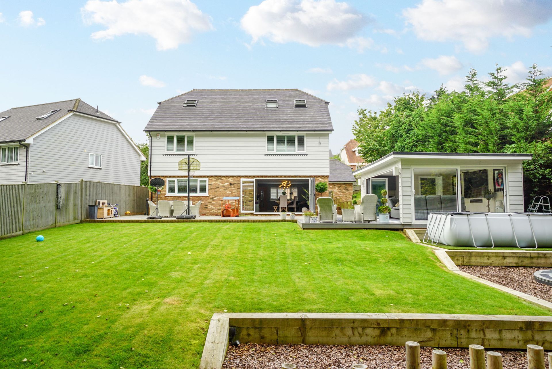 Backyard of a two-story white house with a green lawn, a wooden gazebo, and a gray roof, under a blue sky.
