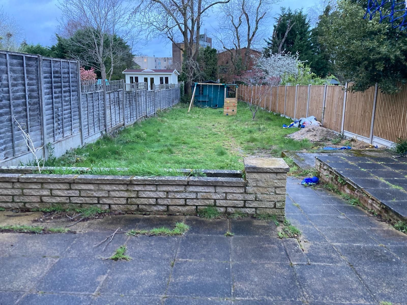 Backyard with overgrown grass, brick wall, and various fences.