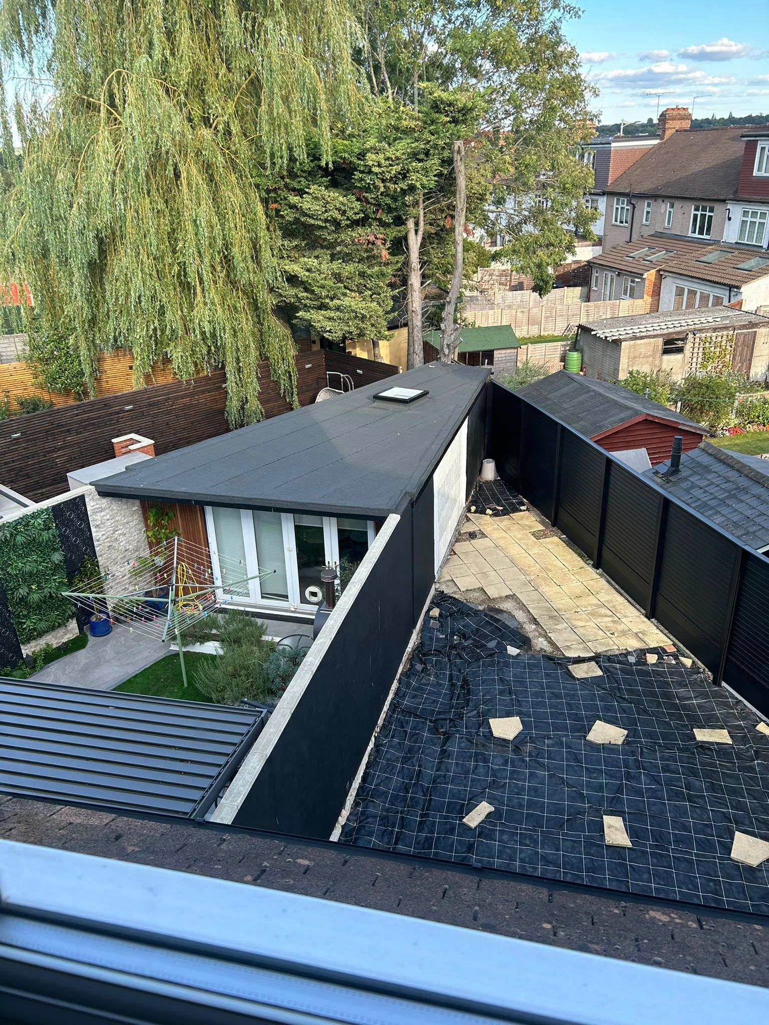 View of a partially re-roofed building, black and gray shingles, with surrounding trees and houses in the background.