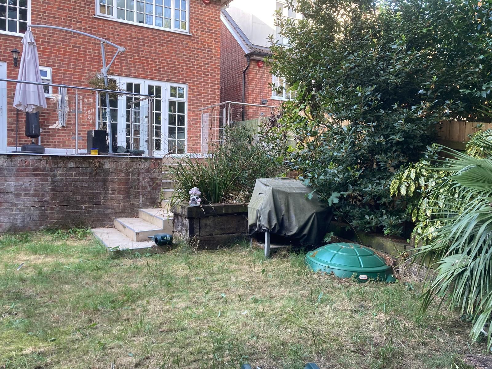 Backyard with brick house, patio, grill under cover, steps, and overgrown grass.