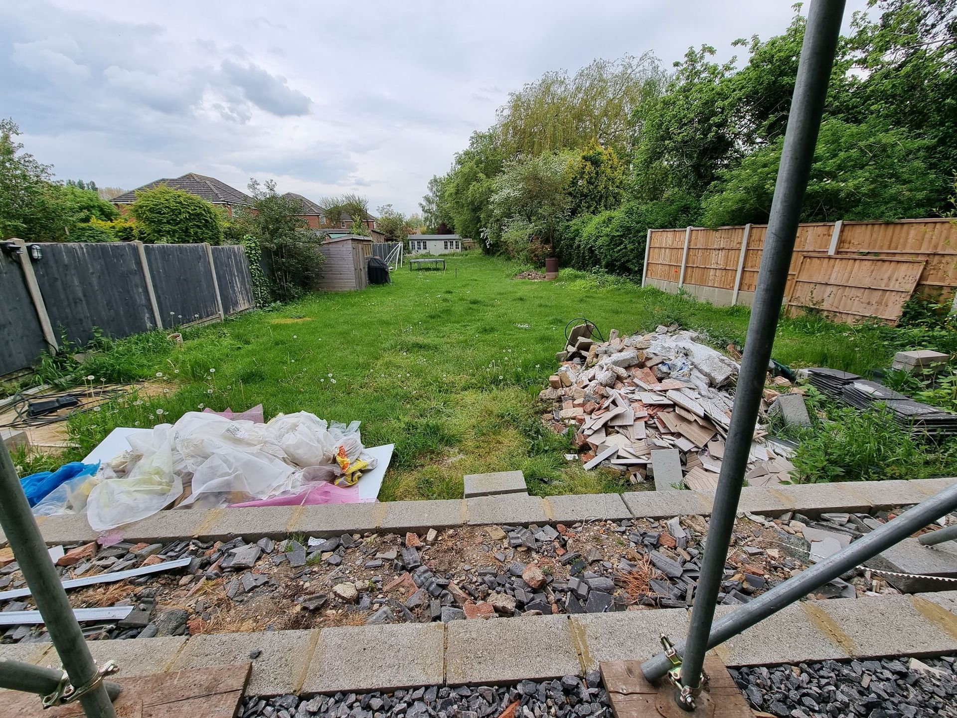 Backyard with grass, debris, and scaffolding; cloudy sky.
