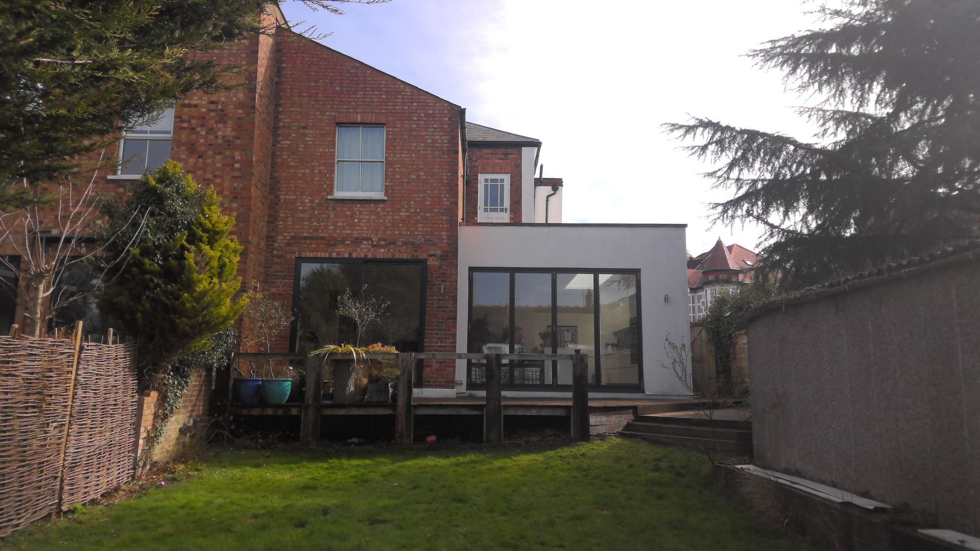 Backyard view of brick house with modern white extension, deck, and green lawn.