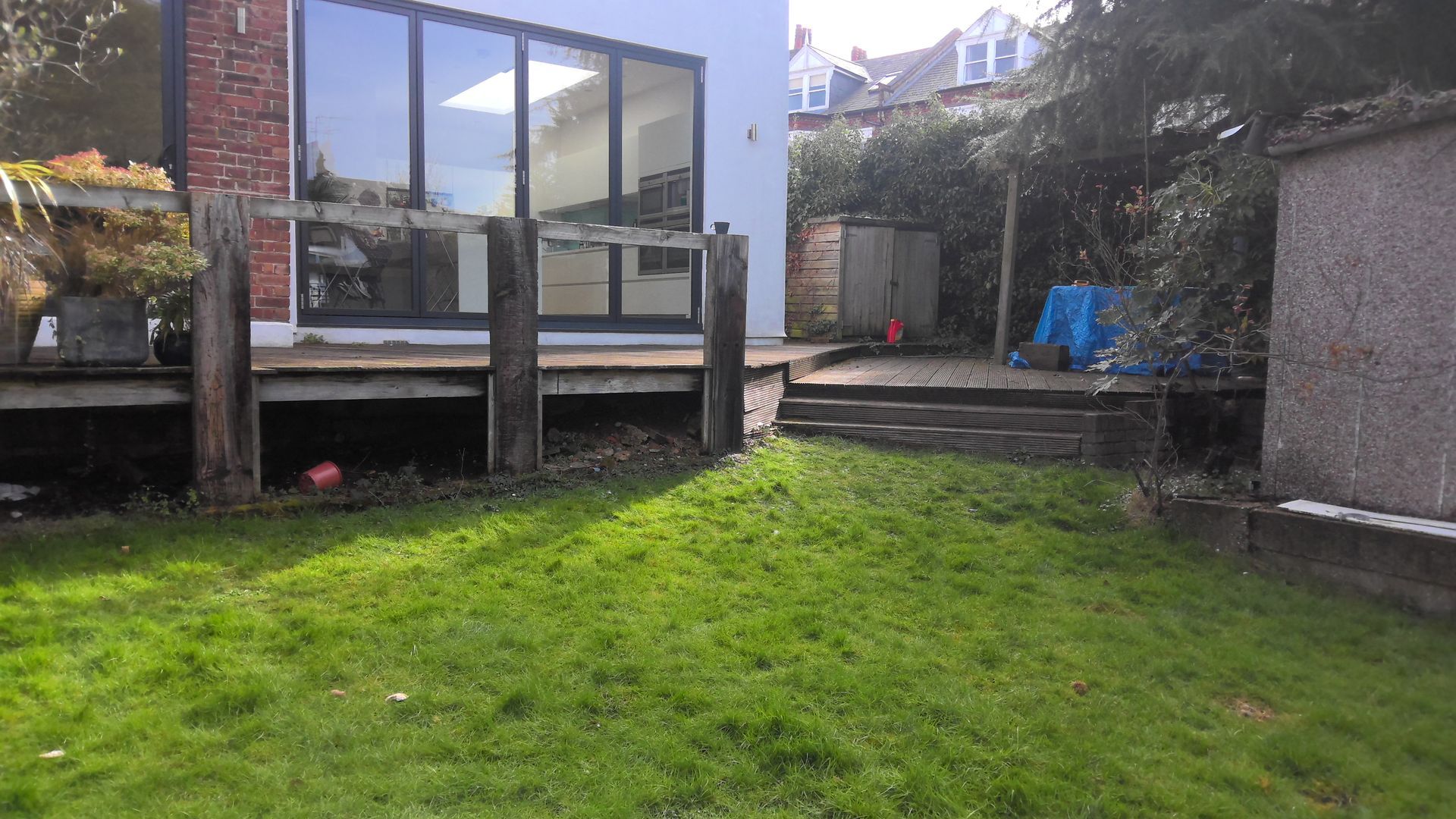 Backyard with grass, wooden deck, large windows, and shed on a sunny day.