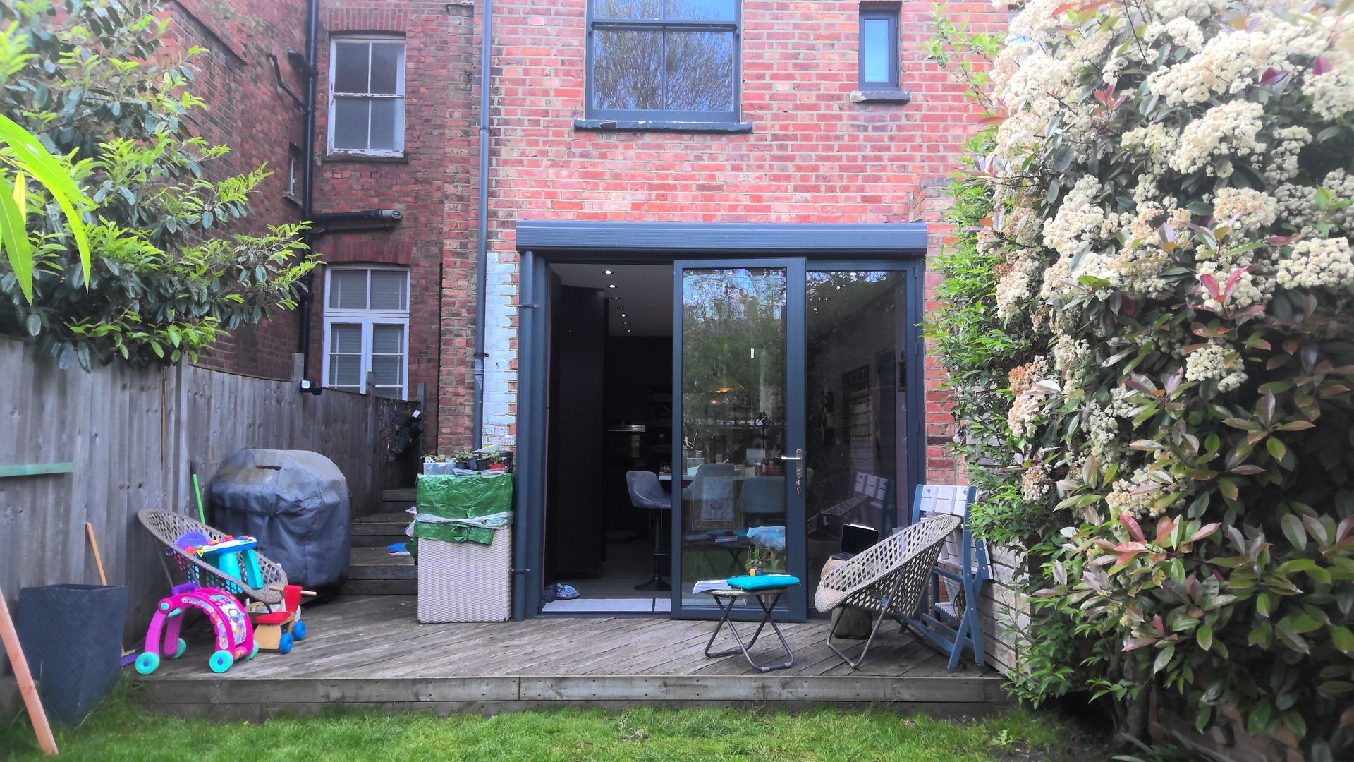 Backyard with a brick building, sliding glass doors, wooden deck, and a green lawn.