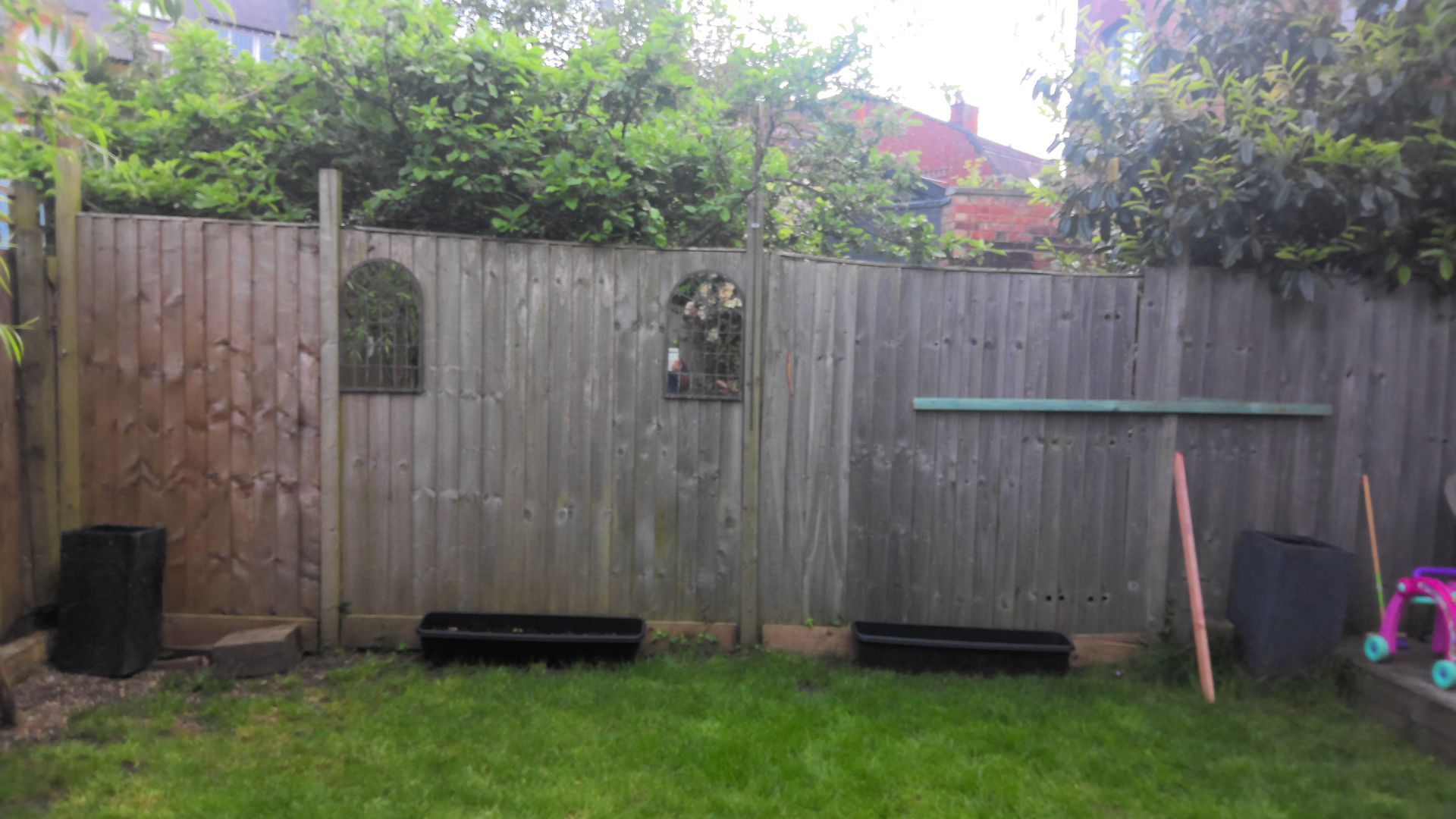 Wooden fence in a backyard with green grass, bushes, and decorative elements.