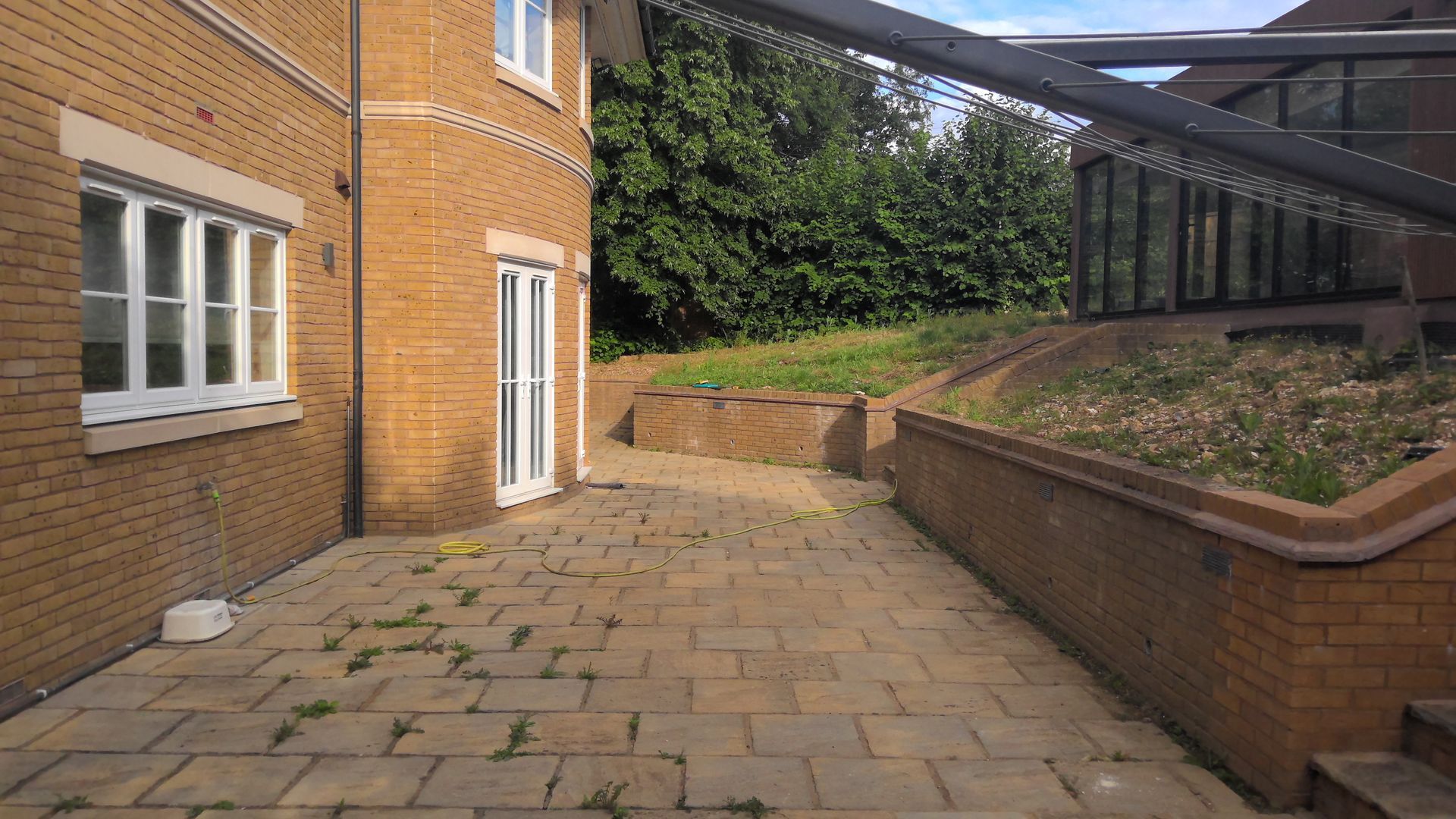 Brick building exterior with a paved walkway, a retaining wall, and overgrown vegetation.