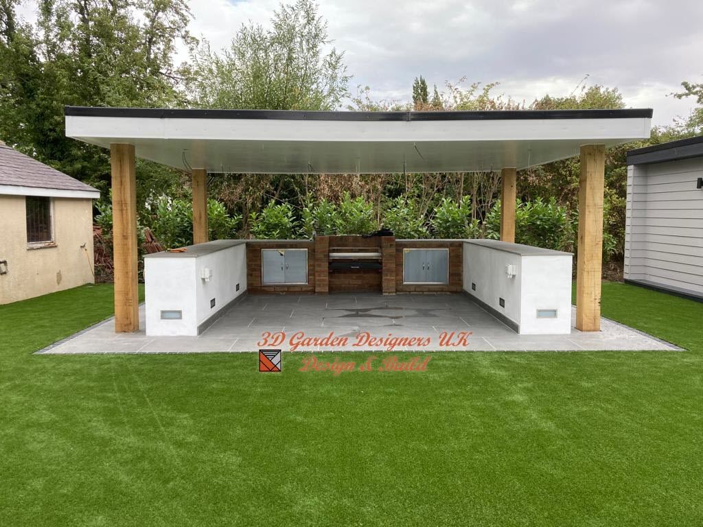 Outdoor kitchen with white cabinets, built-in grill, under a covered wooden structure, on green lawn.