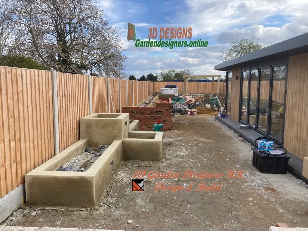 Garden under construction with raised concrete planters and a wooden building, next to a wooden fence.