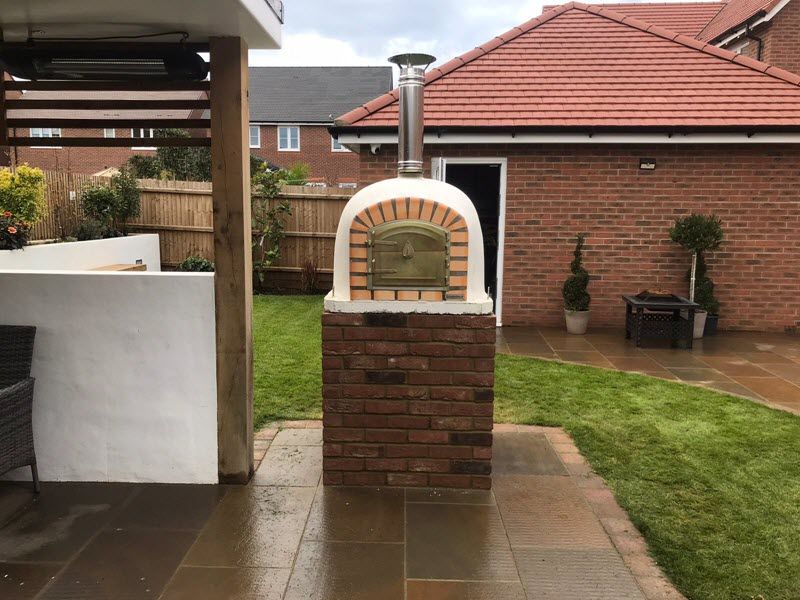Brick pizza oven with stainless steel chimney, in a backyard setting.