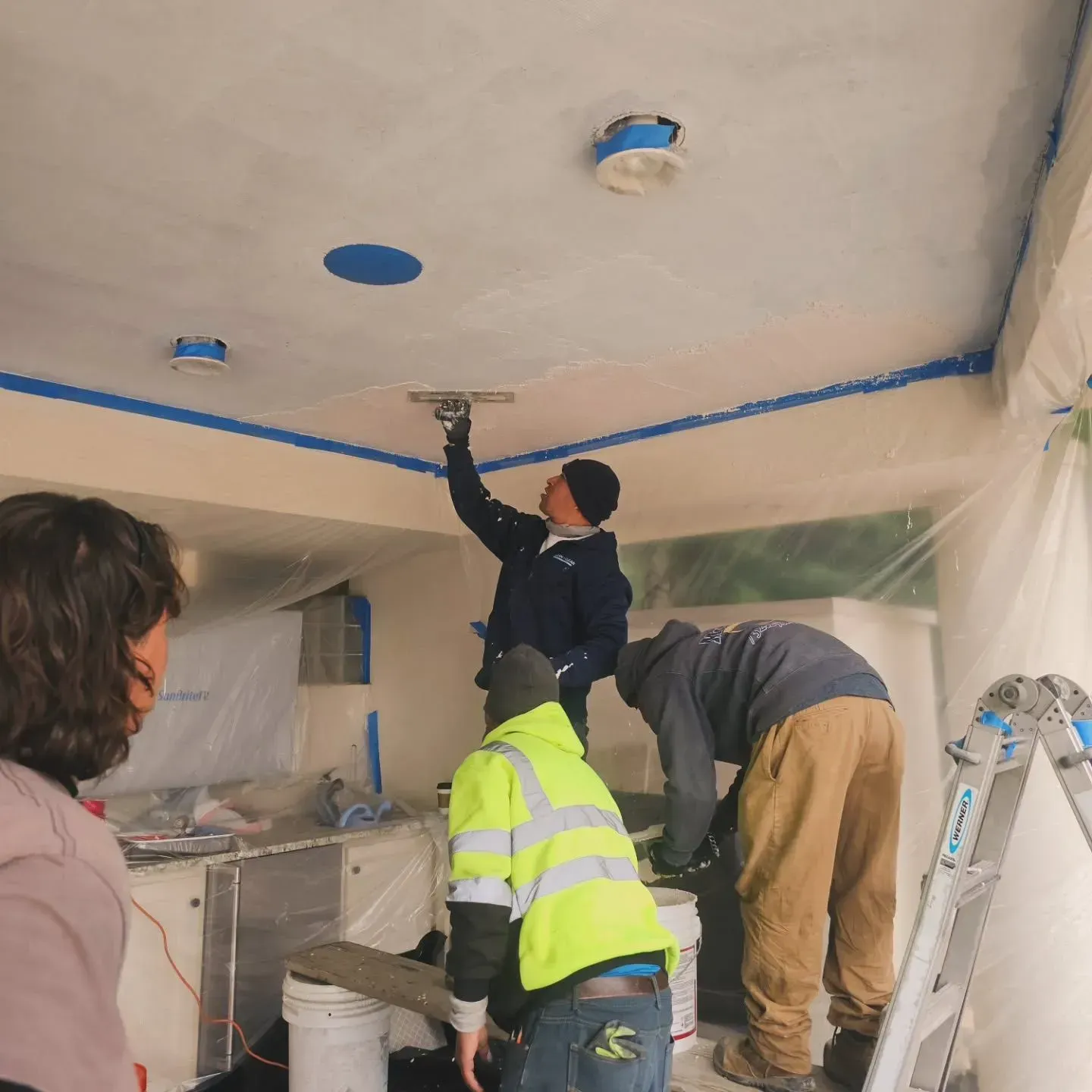 A group of people are working on a ceiling with a ladder in the foreground