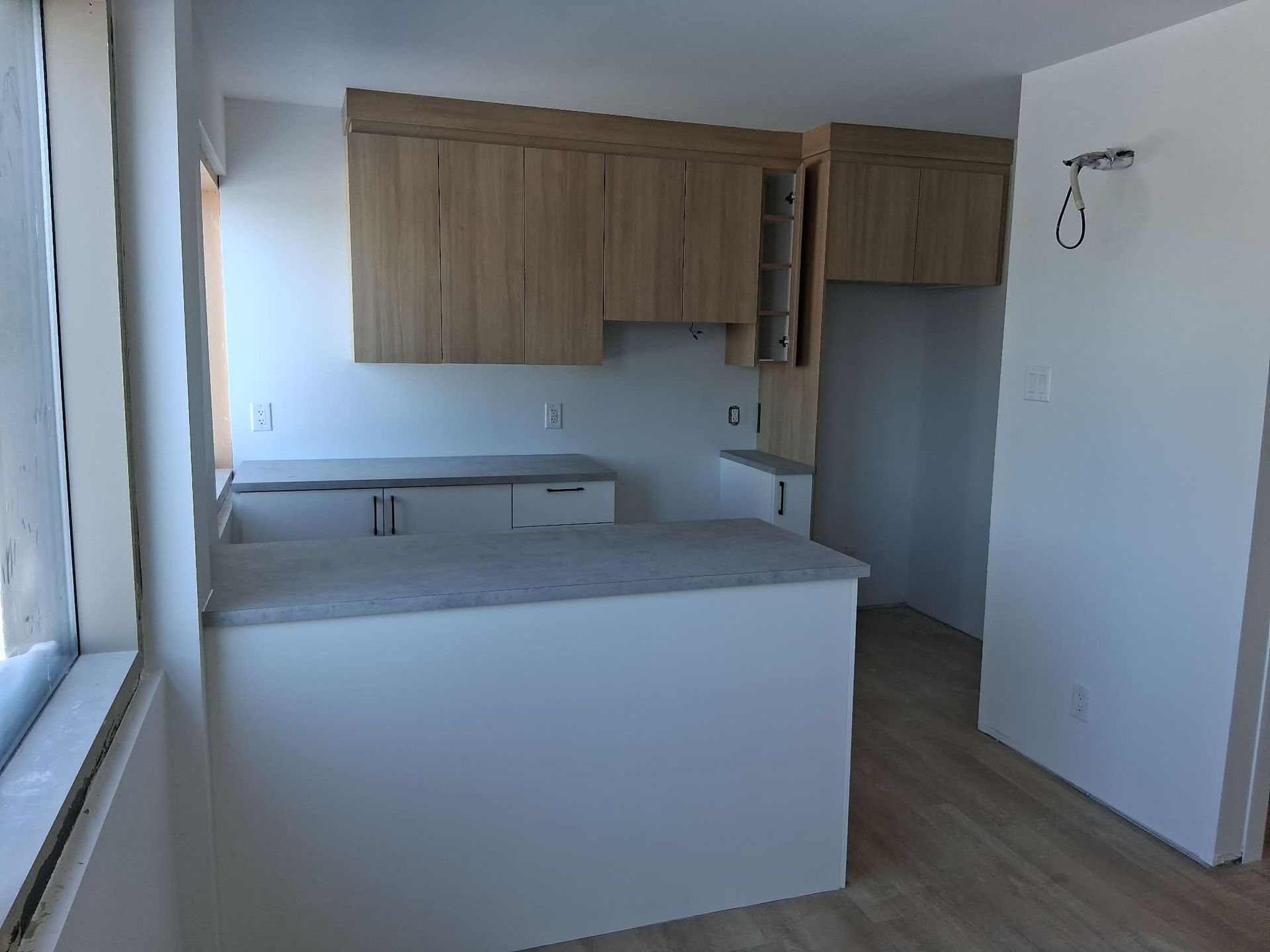 Cuisine vide avec placards en bois clair, plans de travail blancs et murs blancs.