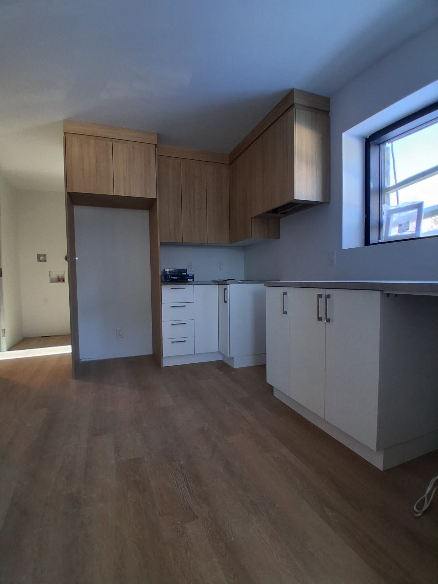 Cuisine récemment rénovée avec placards en bois et blancs, parquet et fenêtre.