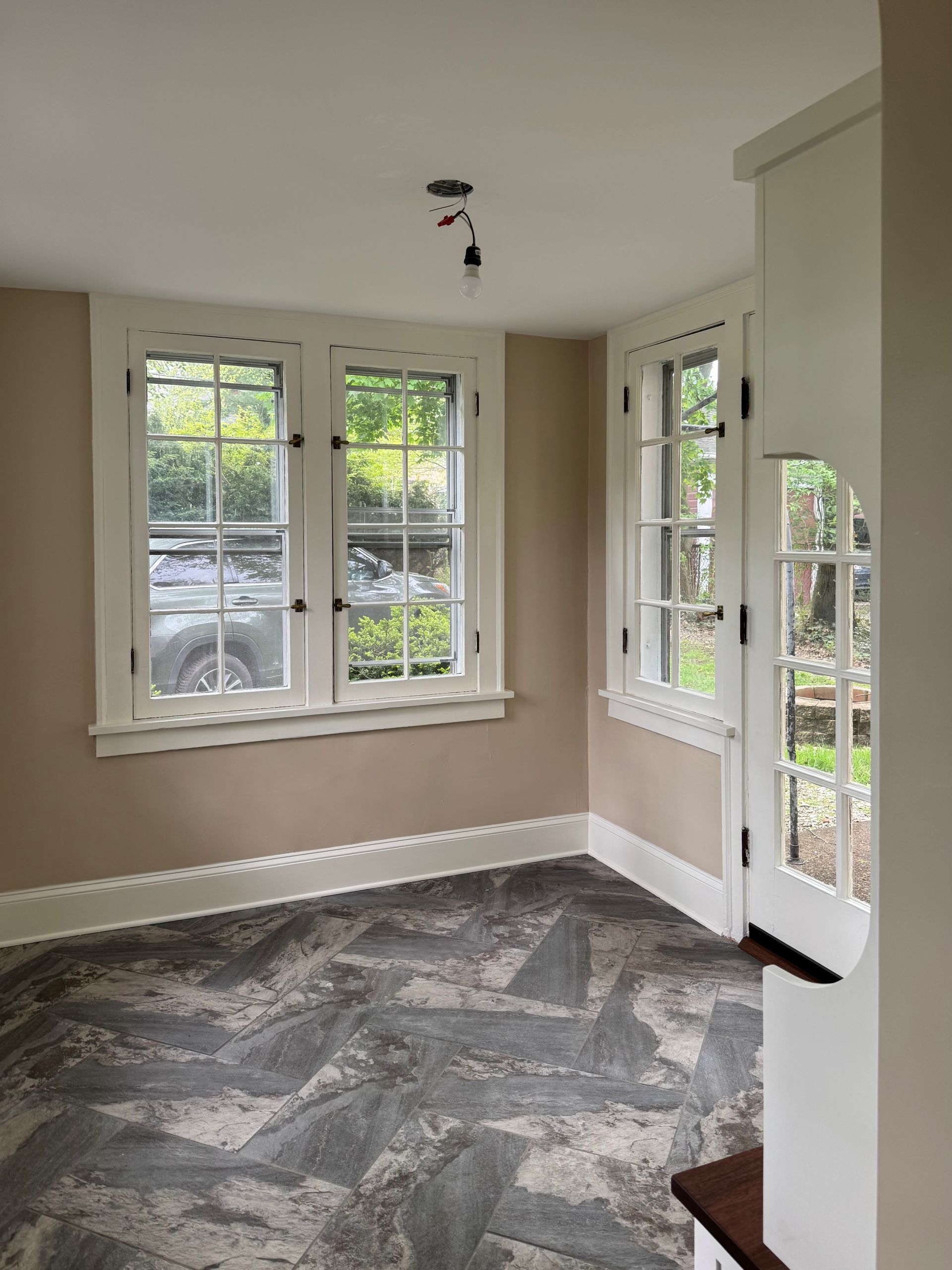 A sunroom with tan walls, white trim, a stone-patterned floor, two large windows, and a glass-paned door.