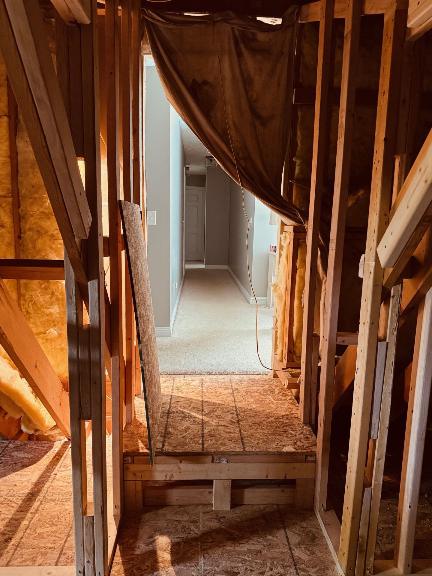 A wooden frame structure under construction, leading to a finished hallway with carpet visible in the background.