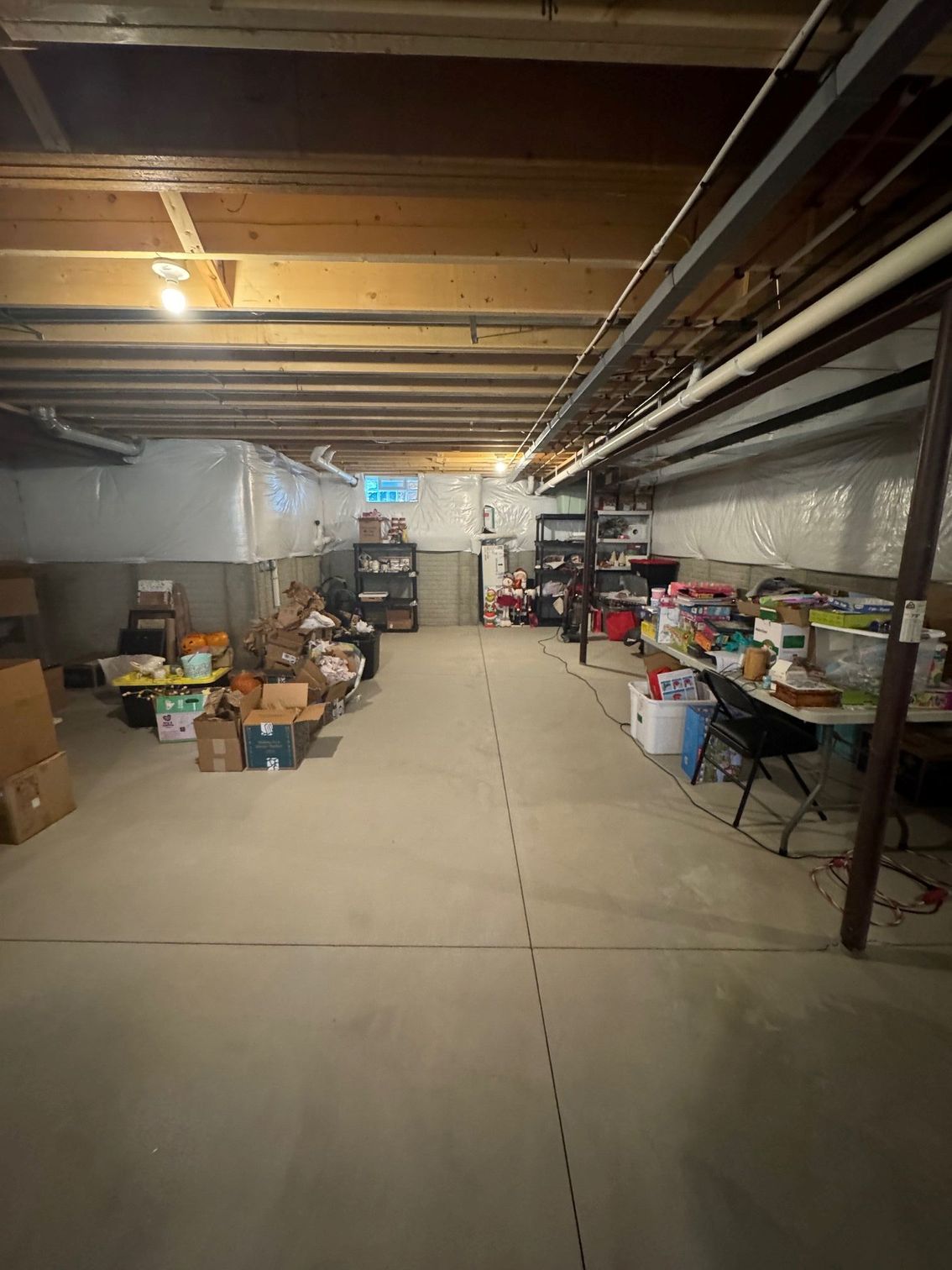 A partially finished basement with exposed wooden ceiling beams, concrete floors, storage shelves, and boxes.