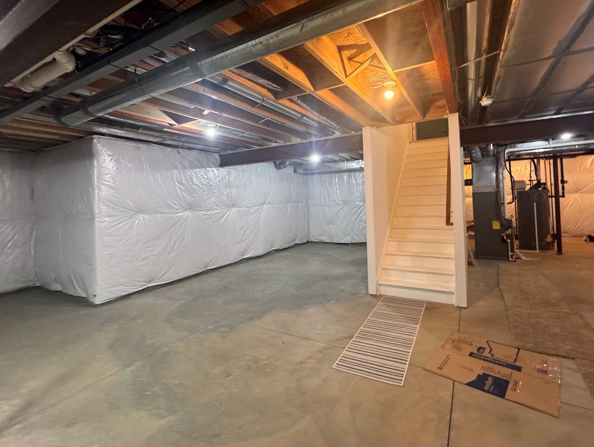 A basement featuring white vapor-barrier walls, a concrete floor, and wooden stairs leading up.