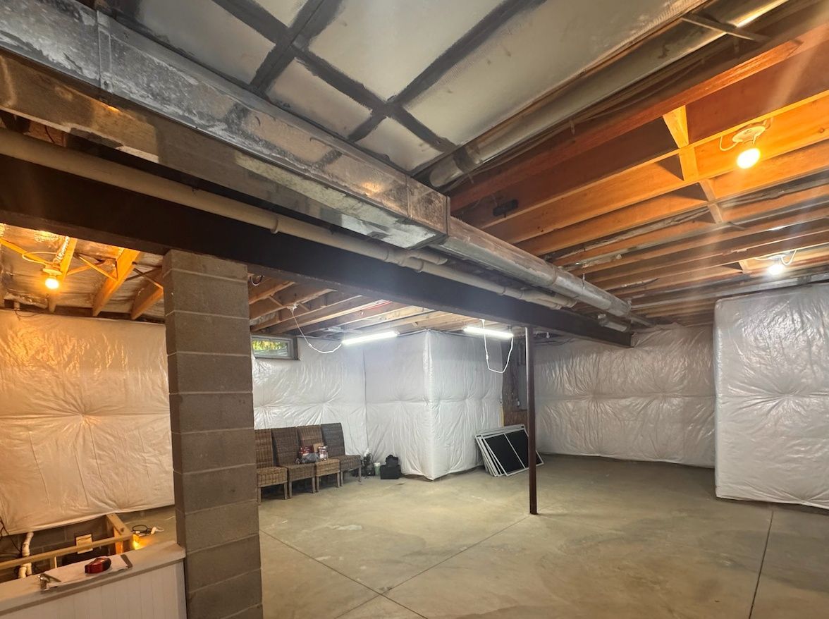 A partially finished basement with insulated walls, exposed ceiling joists, support columns, and concrete flooring.