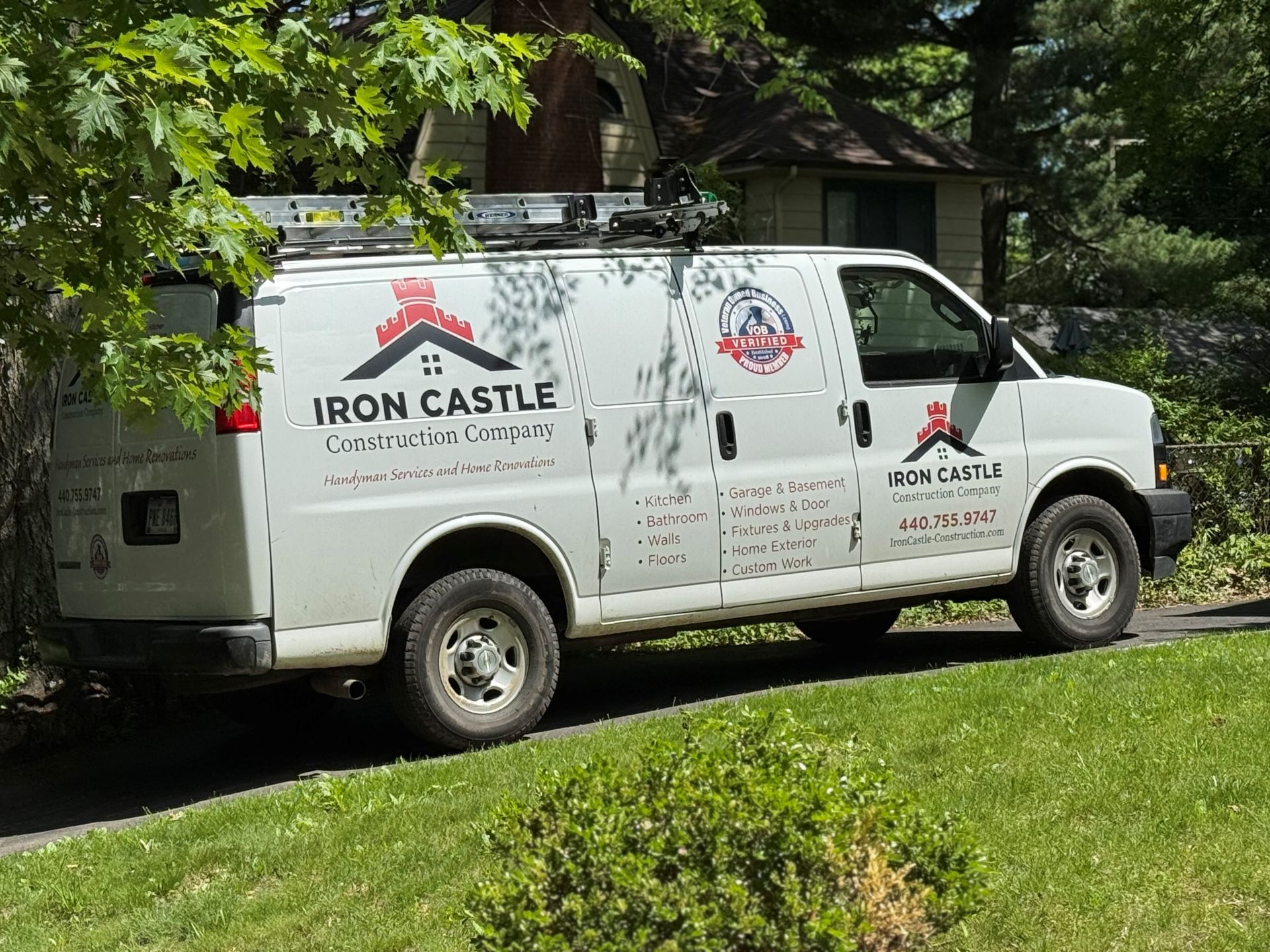 White Iron Castle Construction Company work van parked on a grassy verge next to a tree and a house.
