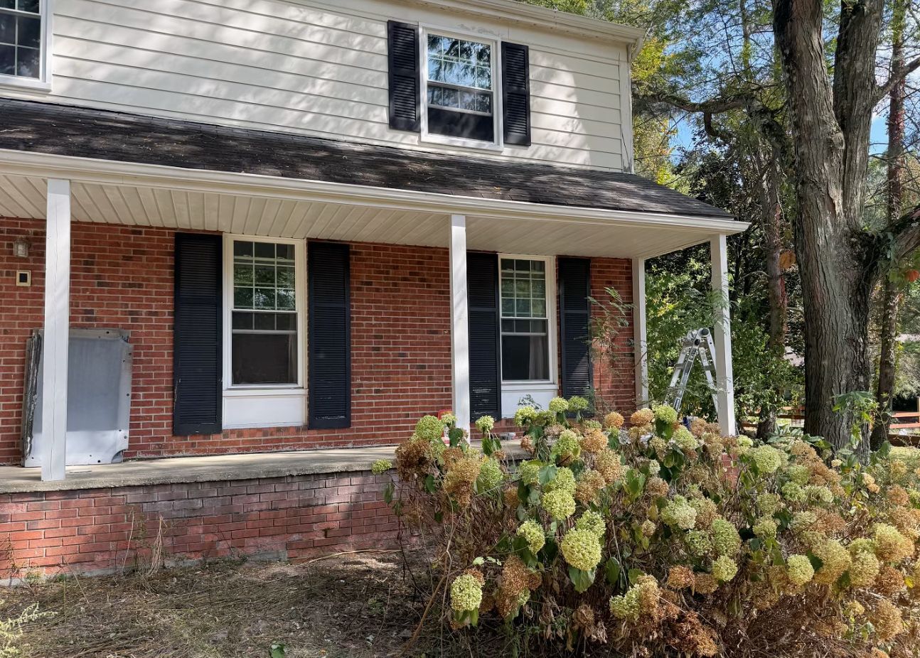 A two-story house with white siding on the top, red brick on the bottom, dark shutters, and a front porch.