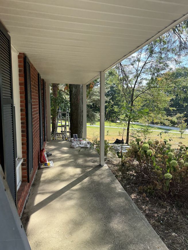 A view from a covered brick porch looking out toward a grassy yard, trees, and a road.