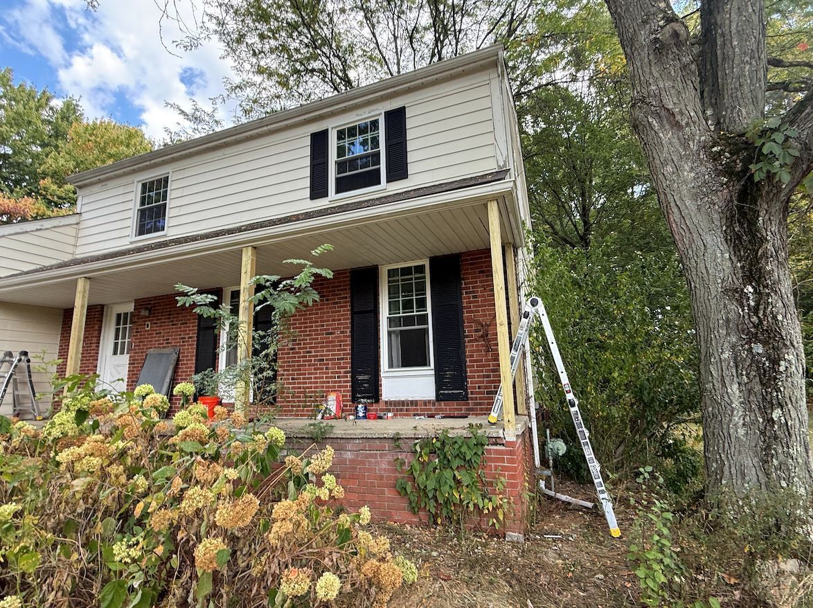 Two-story house with red brick and white siding, featuring a front porch with exposed wooden posts and a leaning ladder.