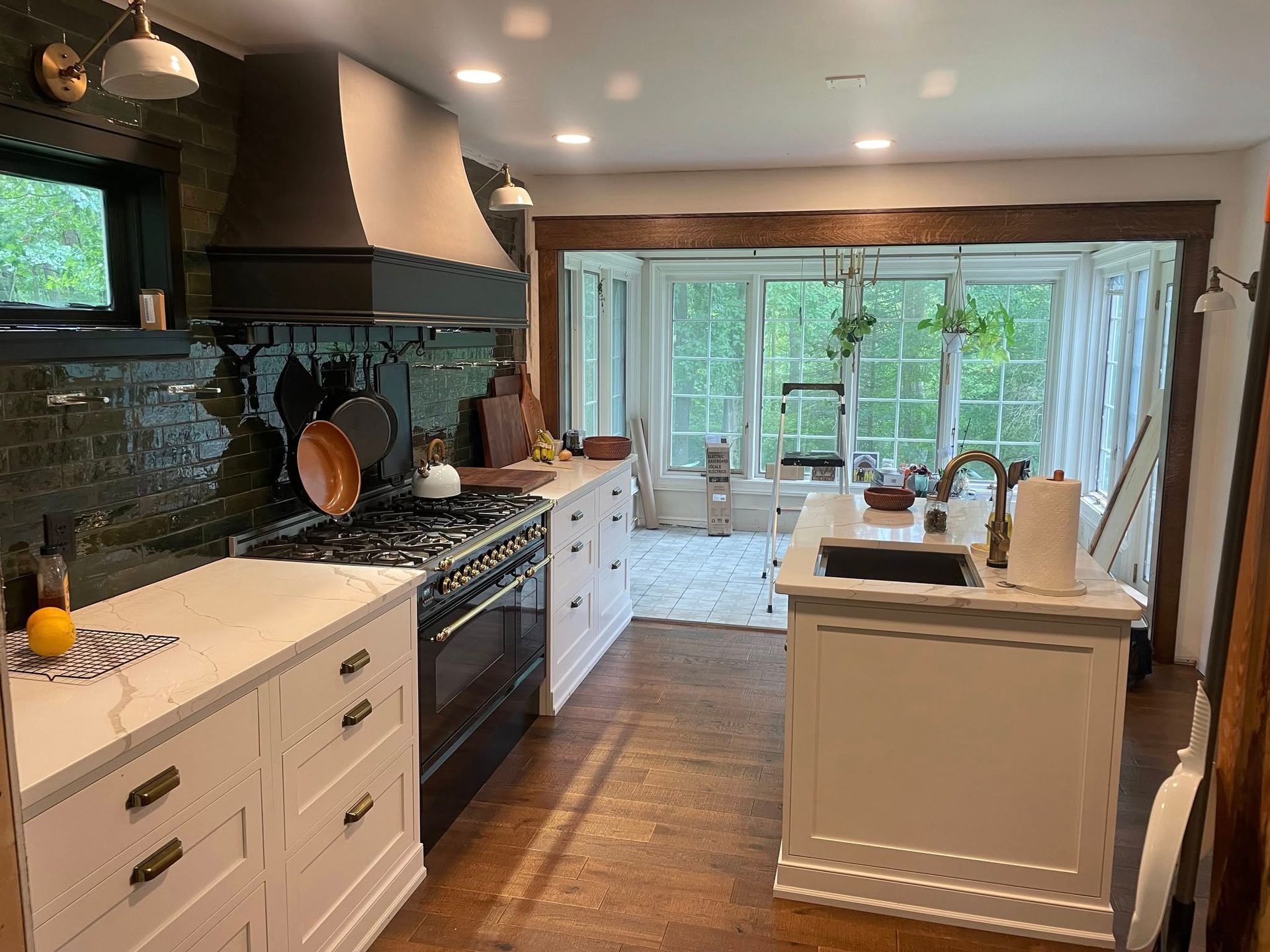 A white kitchen with dark countertops, a large range hood, and a kitchen island, opening into a bright sunroom.