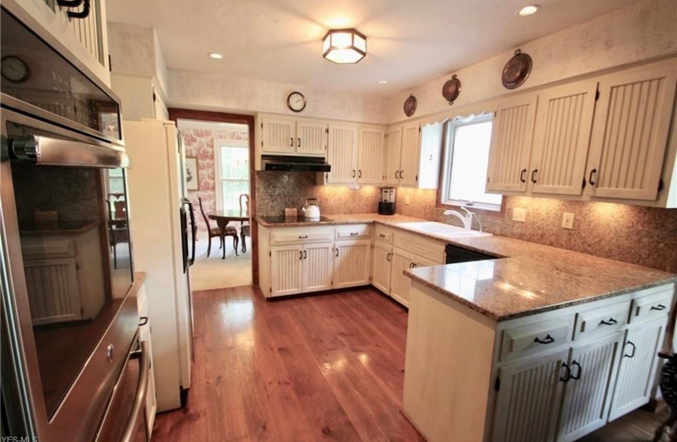 A kitchen with cream-colored cabinetry, granite countertops, wood floors, and a built-in oven, seen from a doorway.