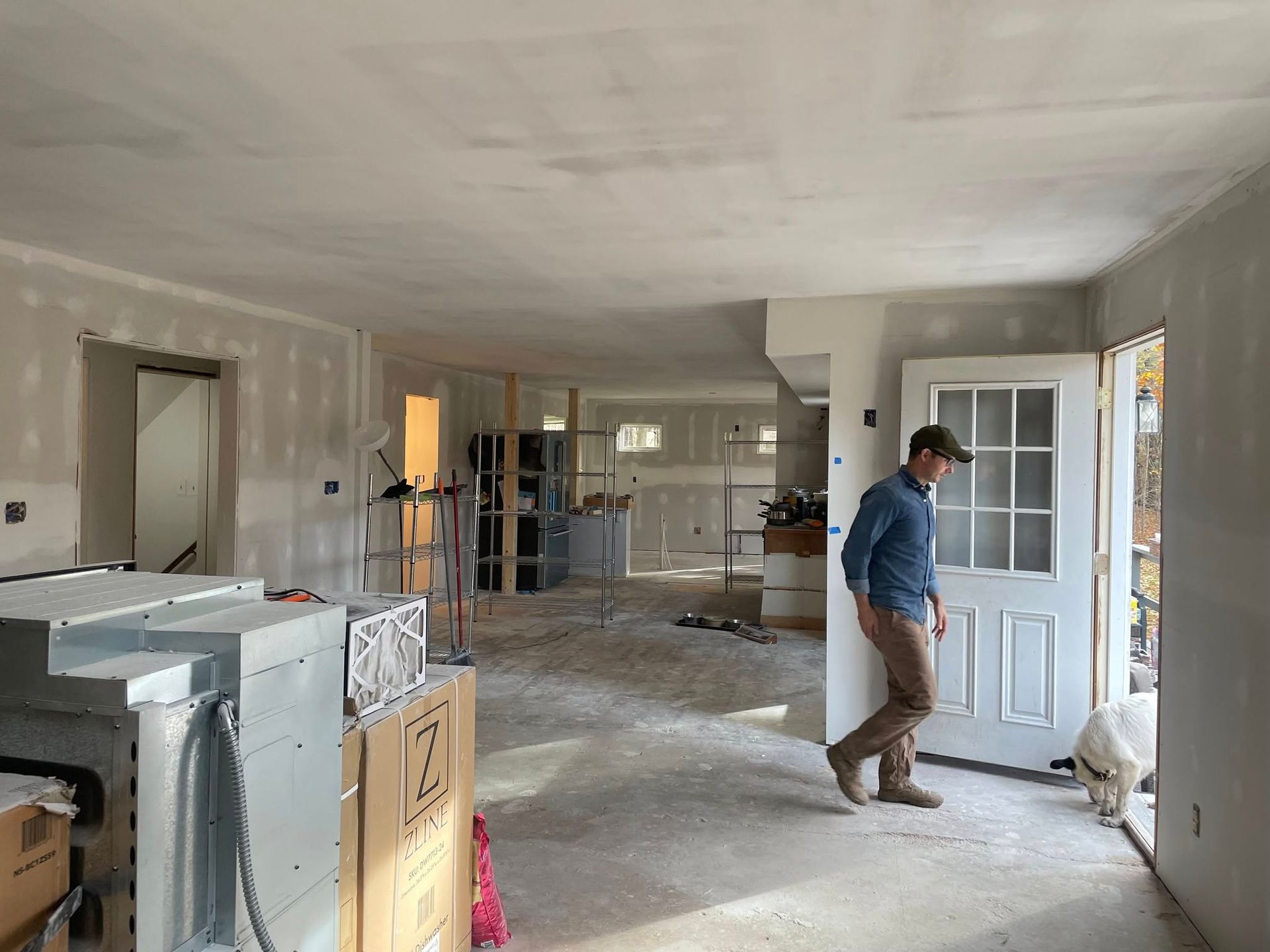 A person in a blue shirt and khaki pants walks through an open doorway into a home renovation site with unfinished walls.