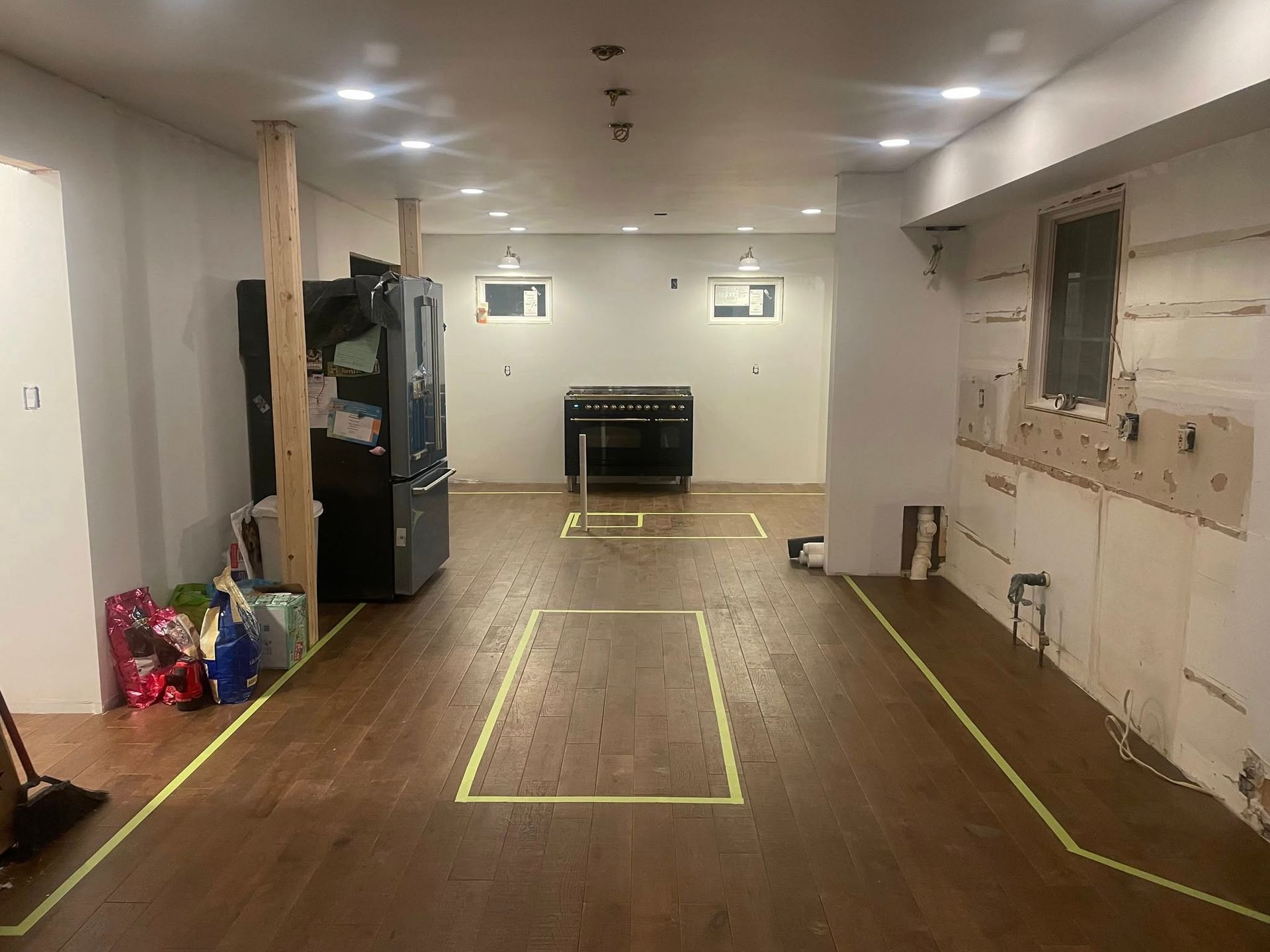 A kitchen undergoing renovation with tape outlines on the floor for cabinets and appliances, and unfinished walls.