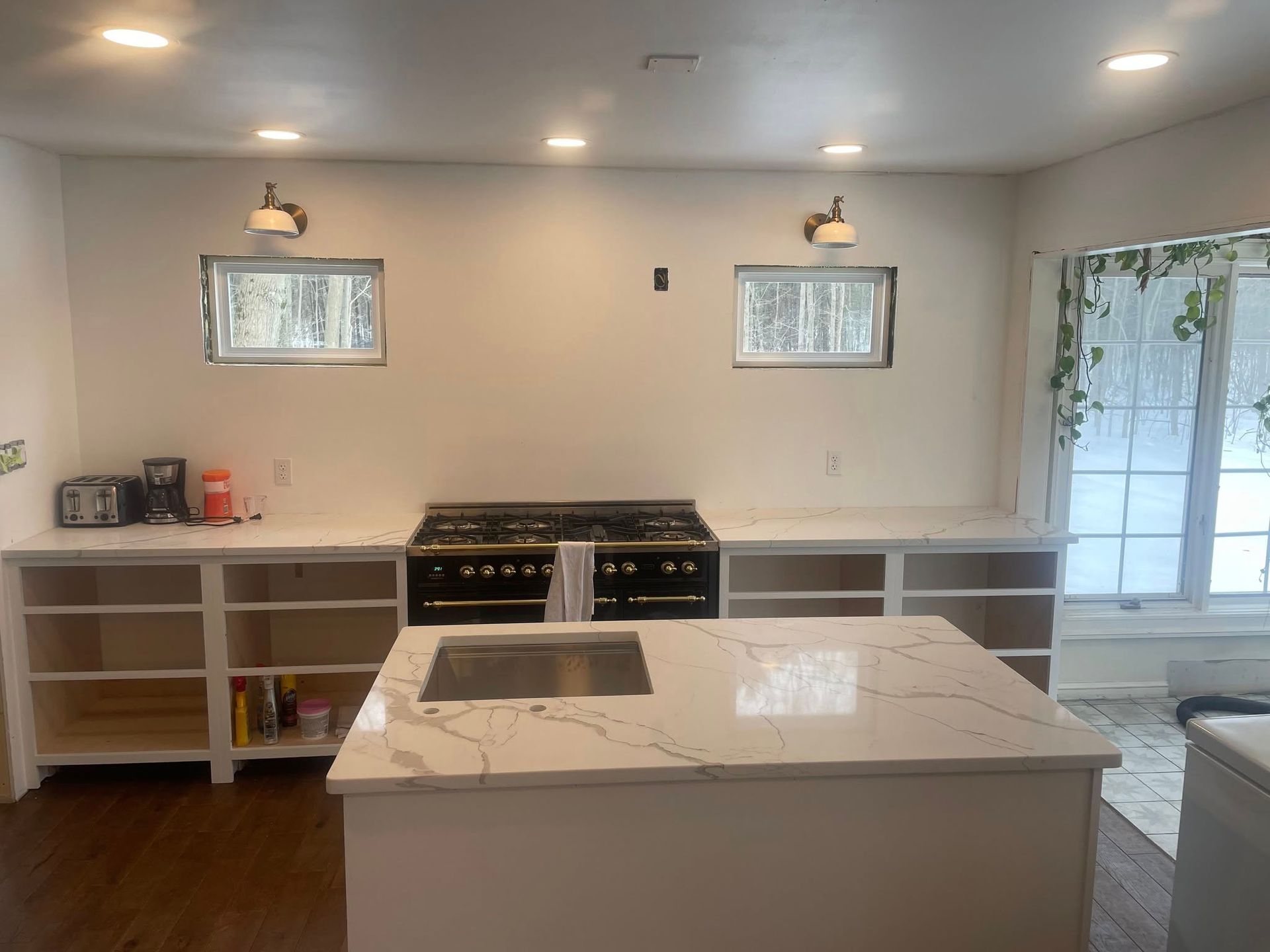 A kitchen renovation featuring white cabinets, a marble-topped island, a black range, and two small windows on a white wall.