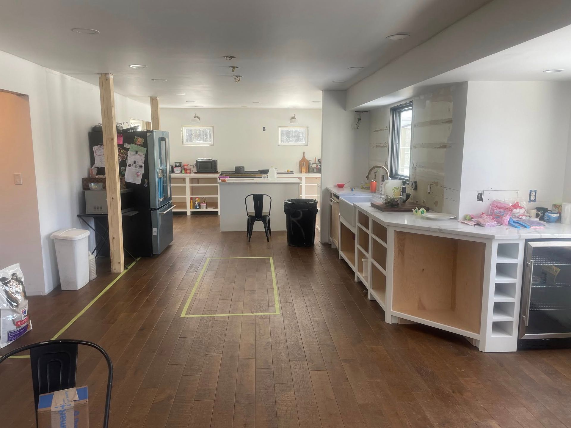 A kitchen undergoing renovation with white cabinets, a large island, wooden flooring, and exposed wooden support posts.