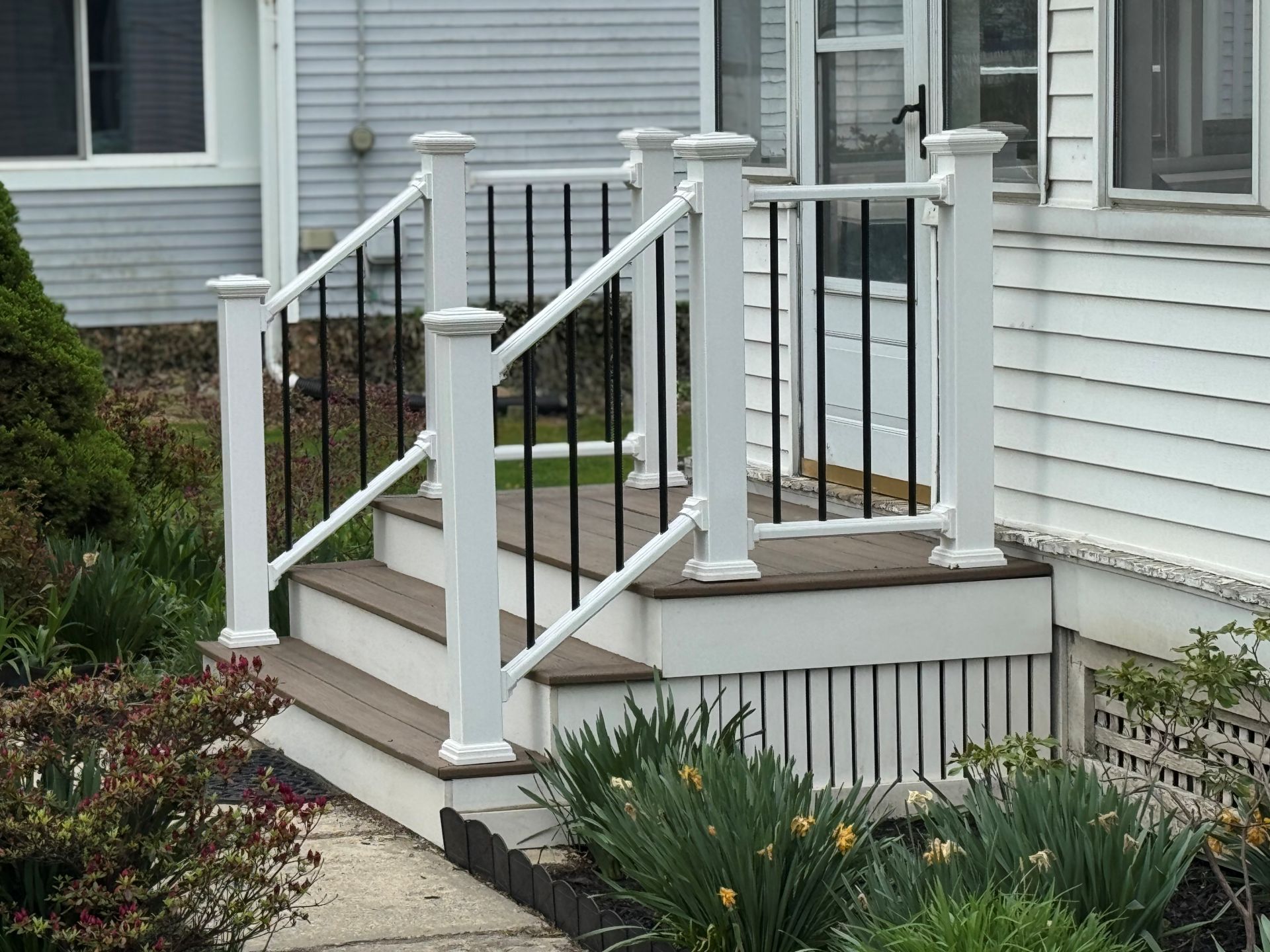 Outdoor staircase with white posts and black railings leading up to a house entrance.
